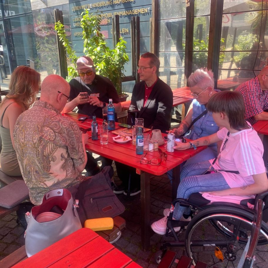 Gruppe von sechs Personen am Tisch mit Getränken und Snacks in einem Freiluftrestaurant.